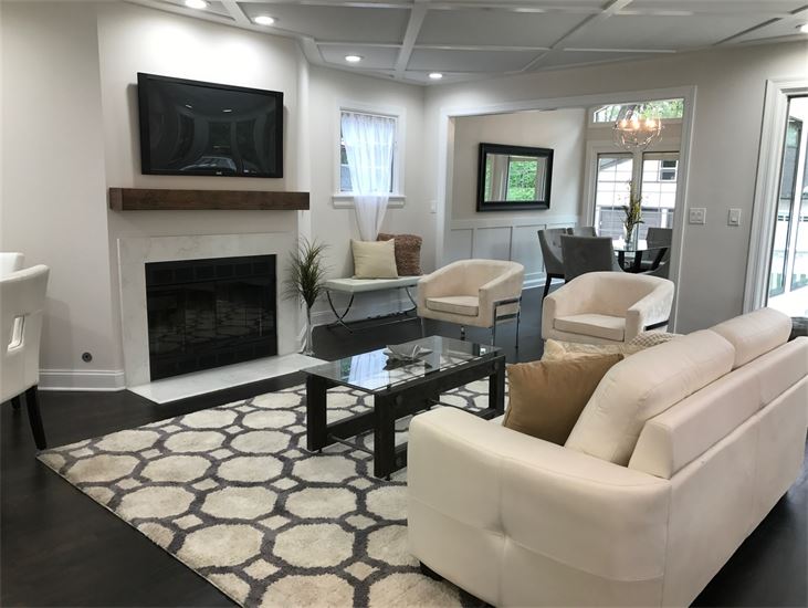Contemporary La Grange living room with dark hardwood floor, white walls, white leather sofa, 2 velvet contemporary accent chairs, coffee table, and dining room with 6 contemporary dining chairs in the background.