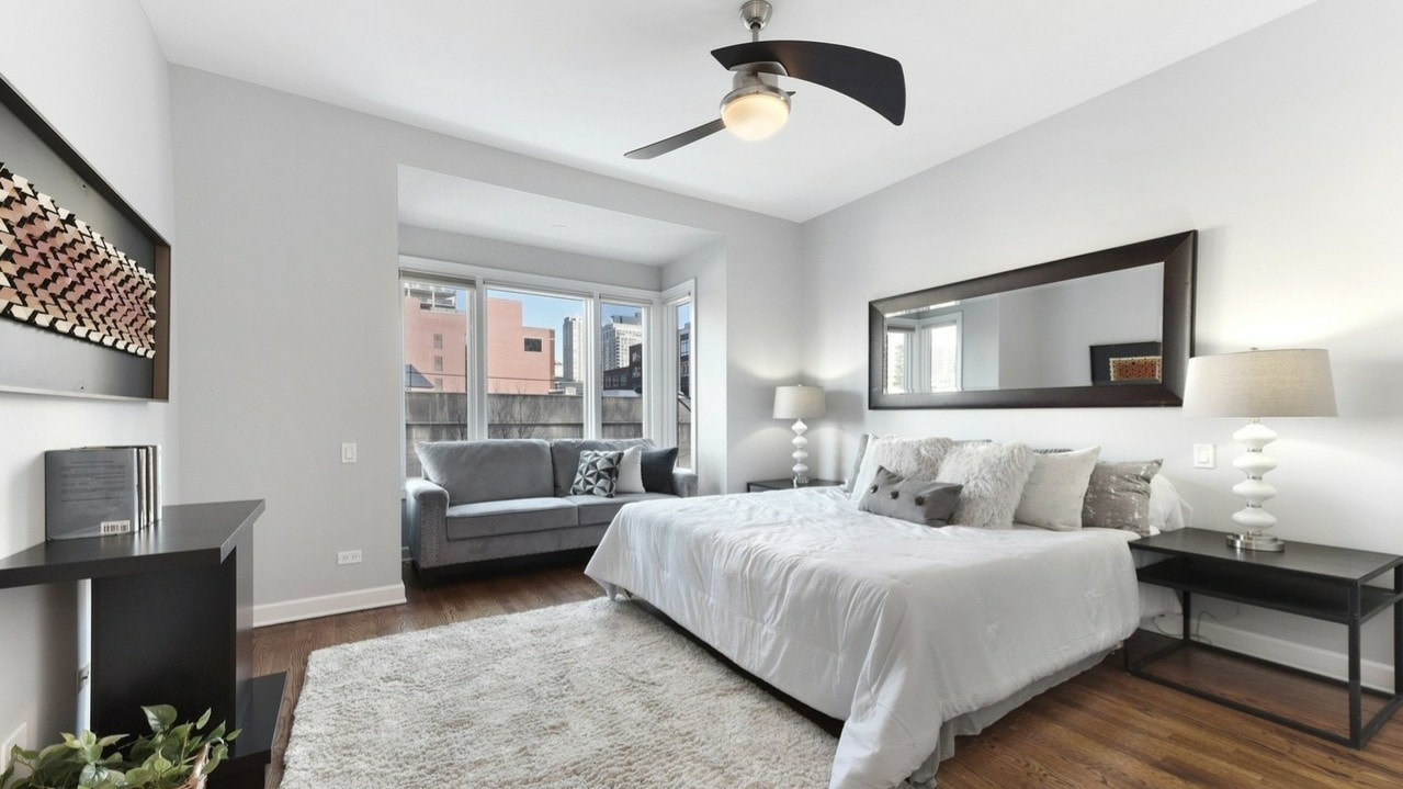 Chicago townhouse primary bedroom with light gray contemporary sofa, king size bed, mirror above the bed, 2 nightstands with matching lamps.